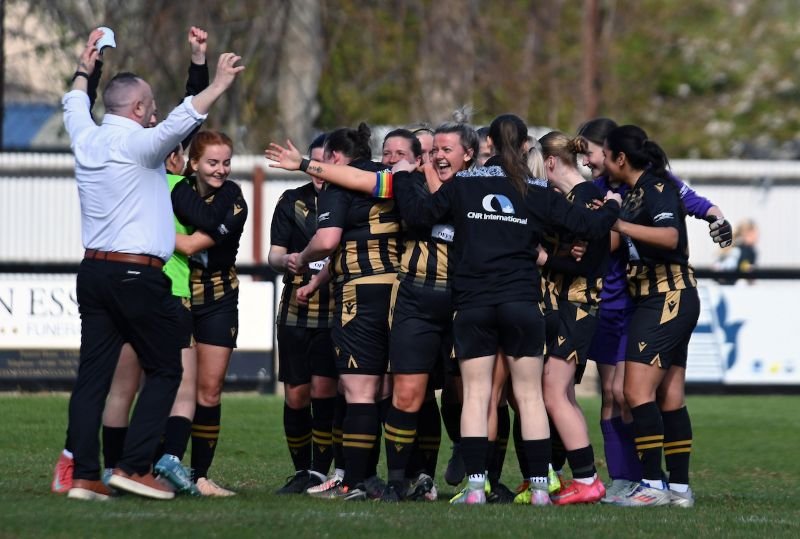 Female soccer team in black and gold celebrate in a tight huddle on the field