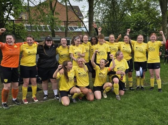 Womens soccer team in yellow uniforms celebrate on a grassy field with one goalie in orange on the left arms raised