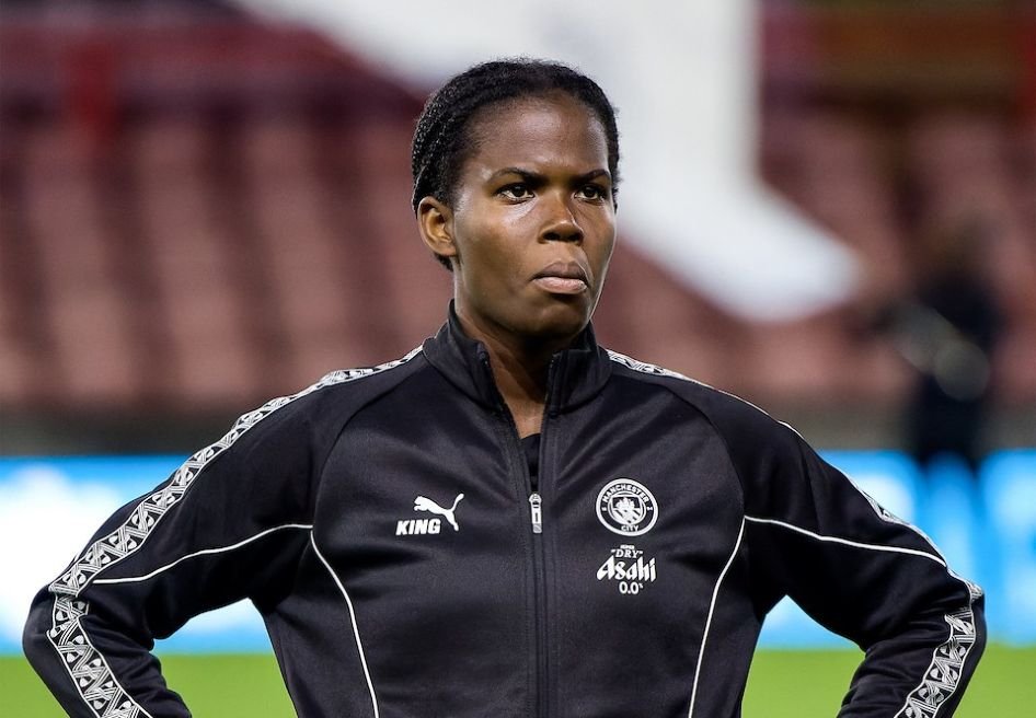 Female soccer player with hands on hips wearing a black training jacket on the field facing forward