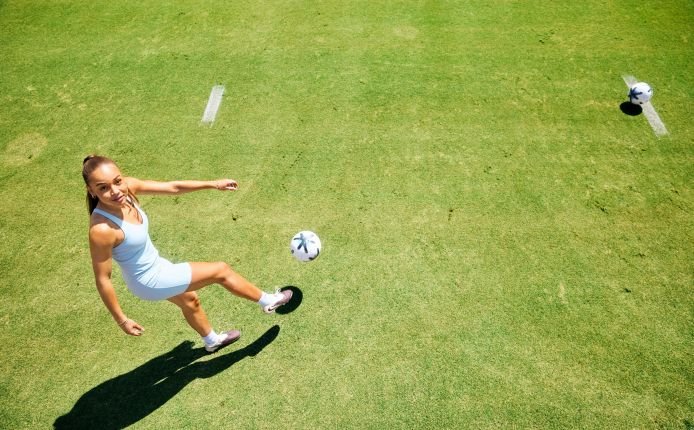 WHM060126FEAsavyking0081logo womensfootballmagazinecom Female soccer player in white kicking a ball on a sunny green field overhead view