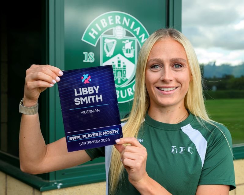 Smiling woman in a green jersey holds a Libby Smith SWPL Player of the Month award in front of a Hibernian crest