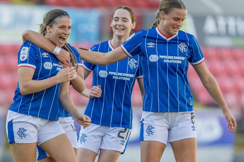 Three female teammates in blue striped soccer jerseys celebrate together on a field
